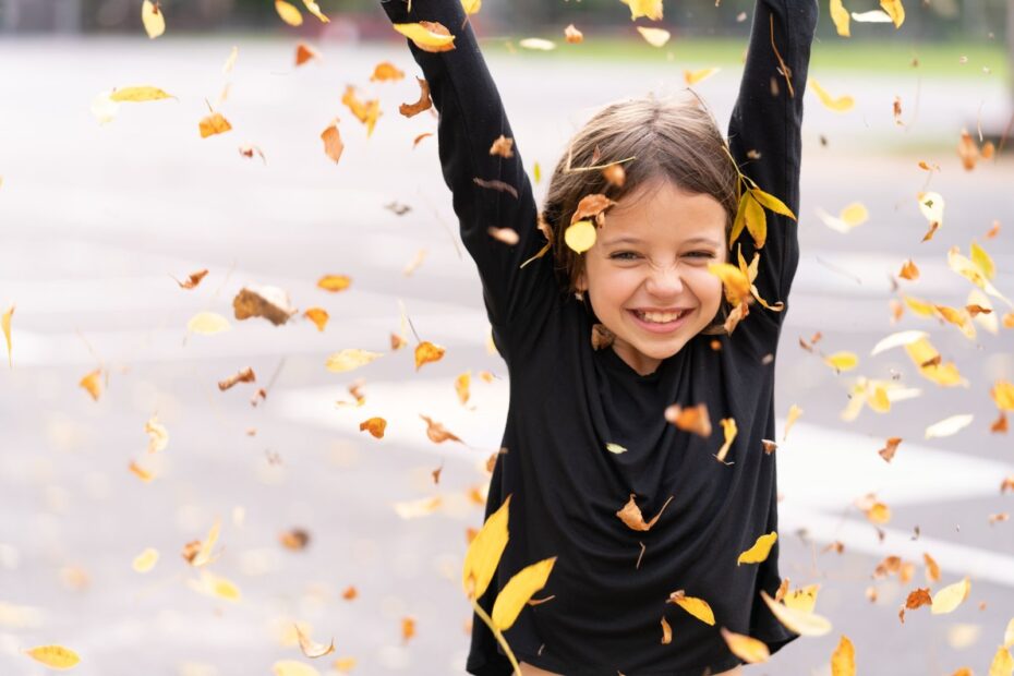 Bambina sorridente che gioca con le foglie all'aperto in un giardino